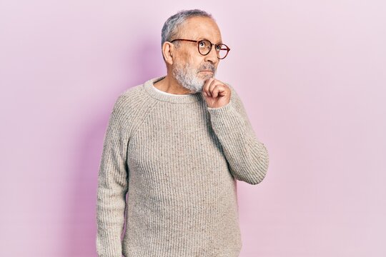 Handsome senior man with beard wearing casual sweater and glasses with hand on chin thinking about question, pensive expression. smiling and thoughtful face. doubt concept.