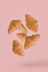 Freshly baked croissants flying in the air isolated on a pastel pink background.