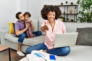 Mother of interracial family working using computer laptop at home smiling friendly offering handshake as greeting and welcoming. successful business.