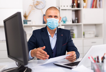 Office worker in a protective mask works behind a laptop