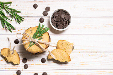 Homemade cookies with chocolate drops  decorated with rosemary branches on white wooden table top view. Tasty homemade dessert on the table.
