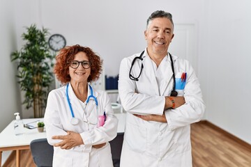 Two middle age doctors at medical clinic happy face smiling with crossed arms looking at the camera. positive person.