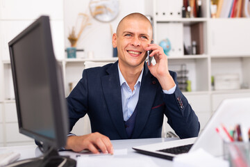 Young man using laptop and talking by phone at the office table