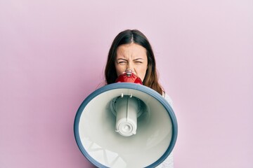 Young brunette woman shouting and screaming through megaphone over pink isolated background