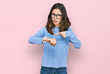 Young beautiful woman wearing casual clothes and glasses in hurry pointing to watch time,...
