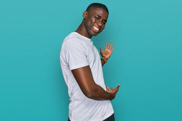 Young african american man wearing casual white t shirt inviting to enter smiling natural with open...