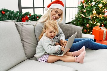 Mother and daughter using laptop sitting by christmas tree at home