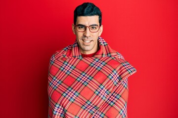 Handsome hispanic man wrapped in a red warm red blanket smiling with a happy and cool smile on face. showing teeth.