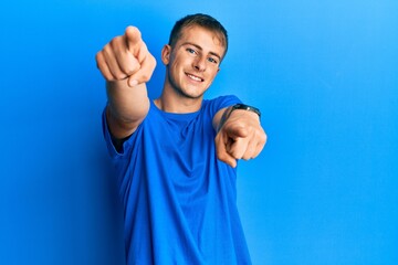 Young caucasian man wearing casual blue t shirt pointing to you and the camera with fingers, smiling positive and cheerful