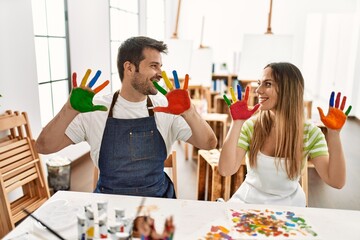 Two hispanic students smiling happy showing colorulf painted hands at art studio.