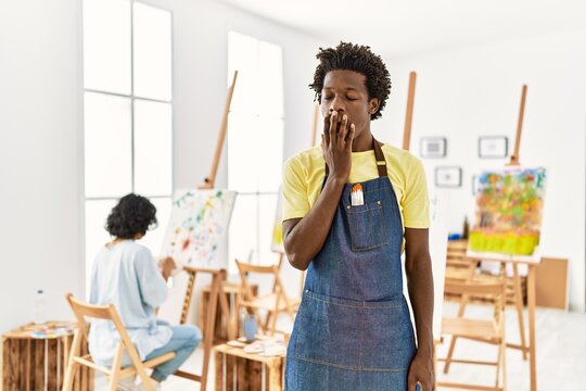 African young man standing at art studio bored yawning tired covering mouth with hand. restless and sleepiness.