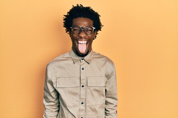 Young african american man wearing casual clothes and glasses sticking tongue out happy with funny expression. emotion concept.