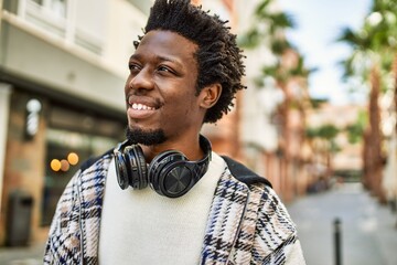 Handsome black man with afro hair wearing headphones smiling happy outdoors