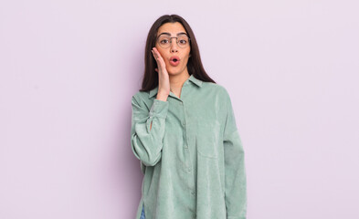 pretty young woman feeling shocked and astonished holding face to hand in disbelief with mouth wide...