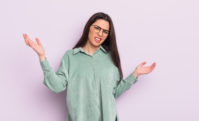 pretty young woman shrugging with a dumb, crazy, confused, puzzled expression, feeling annoyed and...