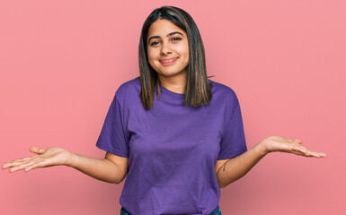 Young hispanic girl wearing casual purple t shirt clueless and confused expression with arms and hands raised. doubt concept.