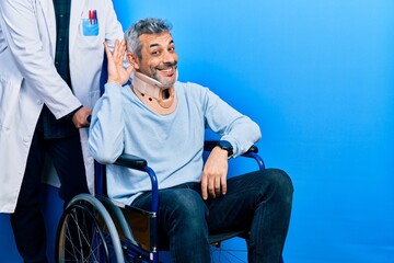 Handsome middle age man with grey hair on wheelchair wearing cervical collar smiling with hand over ear listening an hearing to rumor or gossip. deafness concept.