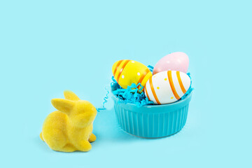 Yellow Easter bunny rabbit with painted egg on plate on blue background.