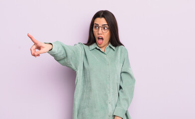 pretty young woman feeling shocked and surprised, pointing and looking upwards in awe with amazed,...