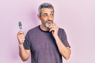 Handsome middle age man with grey hair holding one silver fork serious face thinking about question...