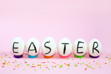 White eggs with black letters EASTER and sweet color sprinkles on a pink background.