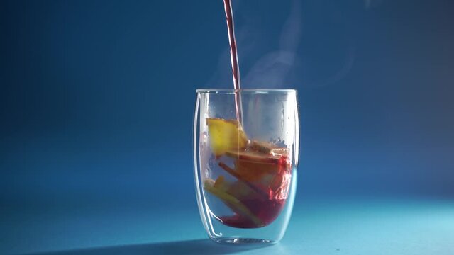 4k video pouring mulled red wine in double glass cup on blue background. Alcohol punch Drink with orange, anise star, cinnamon and apple.