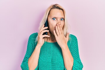 Beautiful caucasian blonde woman having conversation talking on the smartphone covering mouth with...
