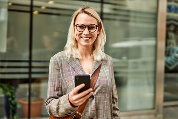 Young blonde businesswoman smiling happy using smartphone at the city.