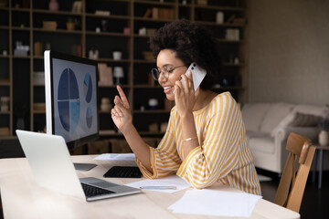 Focused smiling young African American businesswoman in eyeglasses involved in phone call...