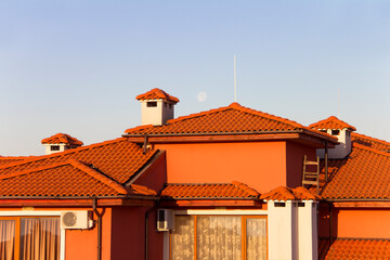 Red tiled roof of a modern multi-storey building. Structures and slopes of roofing surfaces of a building with ventilation systems. Bulgarian architecture on the coast. Properties for sale, for rent.