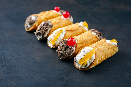 Traditional Italian Sicilian pastry dessert cannoli with creamy ricotta filling, chocolate crisps and fresh currant fruit served as close-up on a rustic black board