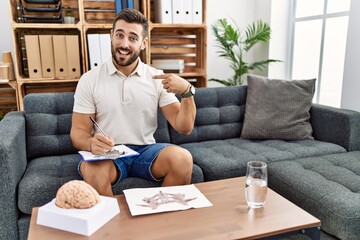 Handsome hispanic man working with rorschach test at psychology clinic looking confident with smile...