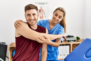 Young hispanic physioterapist woman make arm rehab treatment to man at the clinic.