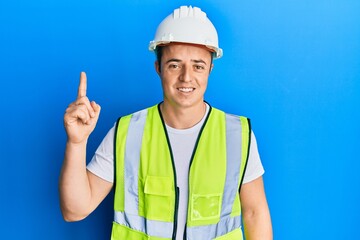Handsome young man wearing safety helmet and reflective jacket pointing finger up with successful...