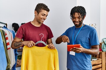 Two men asking shopkeeper for clothes size using touchpad at clothing store