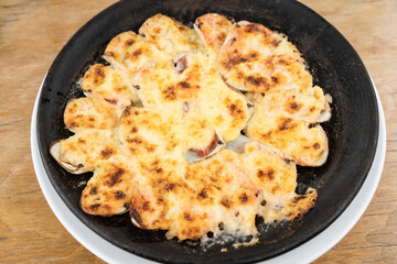 Top view of baked clams covered with parmesan cheese. Closeup on traditional Chilean meal on hot black plate. Gourmet restaurant food concept