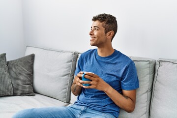 Young hispanic man relaxing sitting on the sofa drinking a coffee at home