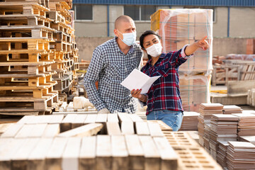 Manager in protective mask gives instructions to the car driver at the building materials storage...
