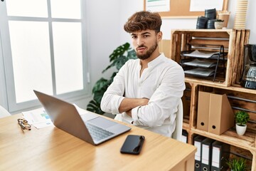 Obraz premium Young arab man working using computer laptop at the office skeptic and nervous, disapproving expression on face with crossed arms. negative person.
