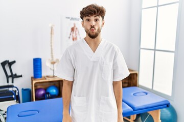 Young arab man working at pain recovery clinic making fish face with lips, crazy and comical gesture. funny expression.