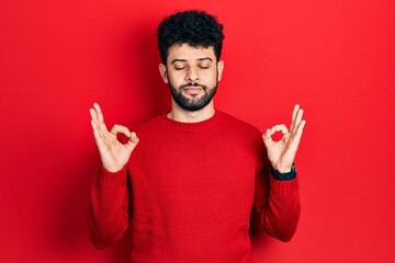 Young arab man with beard wearing casual red sweater relax and smiling with eyes closed doing meditation gesture with fingers. yoga concept.