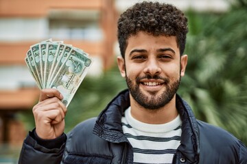 Young arab man holding United Arab Emirates dirham banknotes outdoor at the town