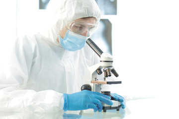 Doctor in a protective suit wearing a mask wearing blue gloves in a laboratory looks through a microscope