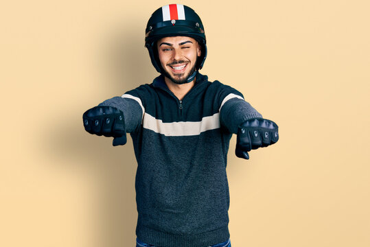 Young hispanic man with beard wearing motorcycle helmet doing driving gesture winking looking at the camera with sexy expression, cheerful and happy face.