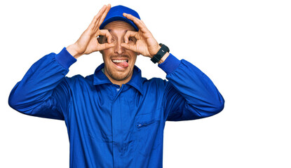 Naklejka premium Bald man with beard wearing builder jumpsuit uniform doing ok gesture like binoculars sticking tongue out, eyes looking through fingers. crazy expression.