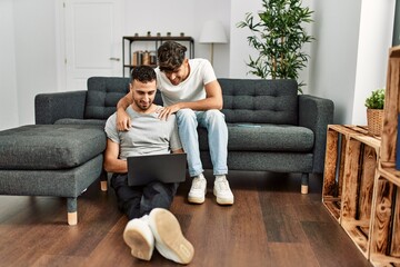 Obraz premium Two hispanic men couple using laptop hugging each other at home
