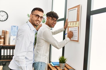 Two hispanic men couple writing on corkboard working at office