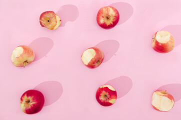 Fototapeta na wymiar Half eaten organic red apples on pastel pink background. Spring summer design for healthy nutrition lifestyle. Creative concept for vitamins commercial.