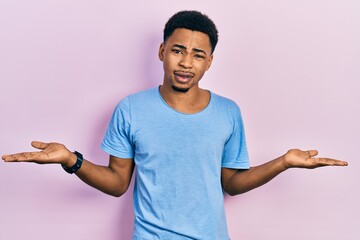 Young african american man wearing casual blue t shirt clueless and confused with open arms, no...