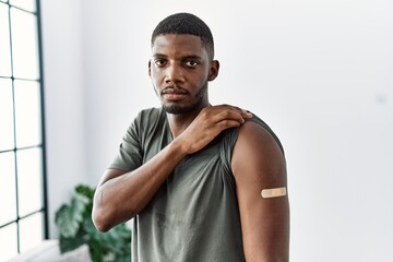 Young african american man getting vaccine showing arm with band aid thinking attitude and sober expression looking self confident